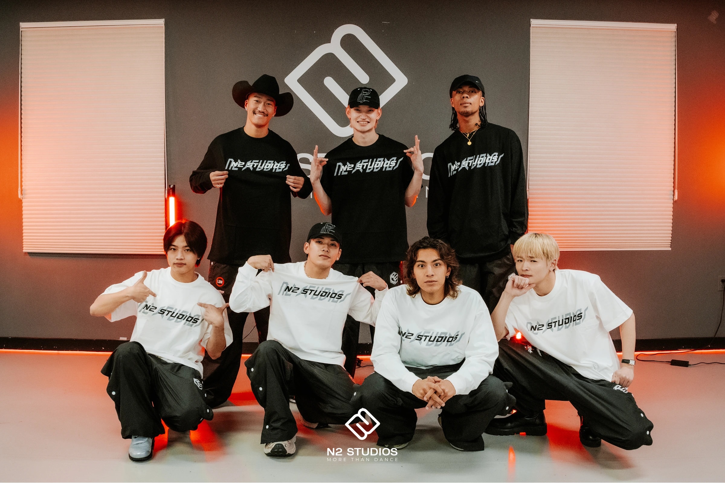 Seven guests posing in N2 Studios shirts in front of the studio logo.