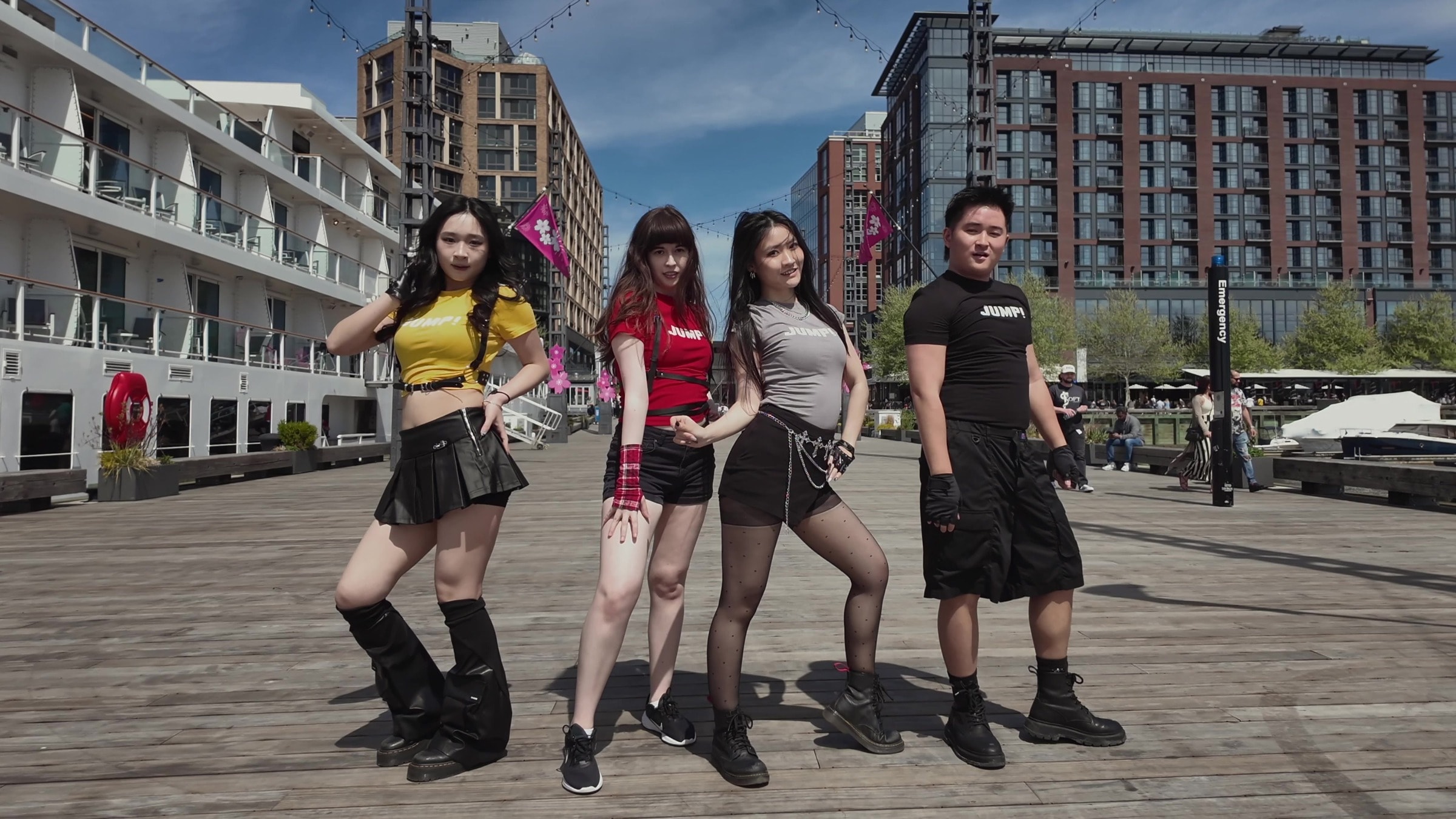 Four N2DC dancers holding the final JUMP formation on a waterfront boardwalk in daylight.